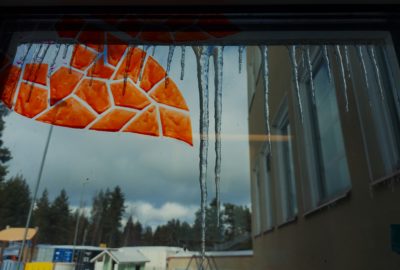 Window display of a red heart shaped artwork. Photo taken from in the building, yard in the background.