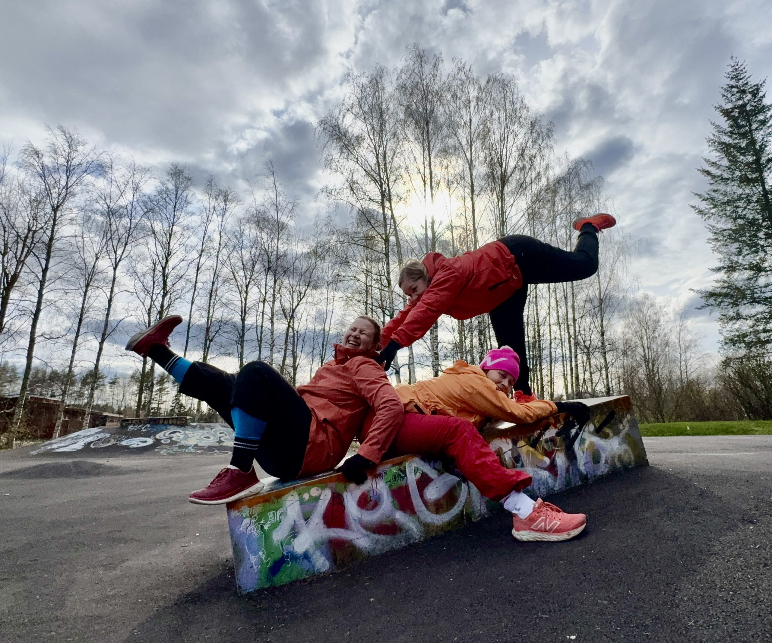 Kolme täti-parkourharrastajaa venyttelemässä skeittipuistossa. Kaikilla punaiset ulkoiluvaatteet.