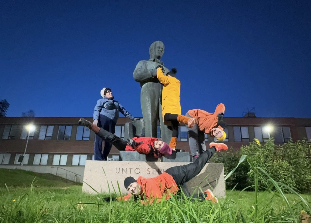 Viisi täti-parkourharrastajaa venyttelemässä patsaan päällä.